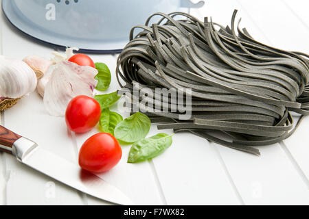 Les nouilles, l'ail, les tomates et les feuilles de basilic sur tableau blanc Banque D'Images