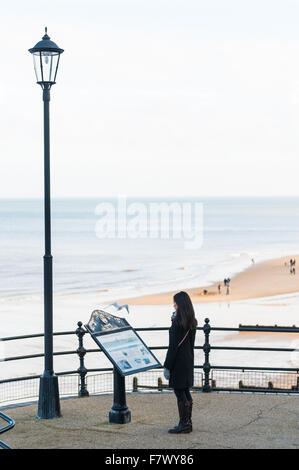 Une jeune femme donne sur la plage et la mer à partir du chemin à côté de la jetée de Cromer Norfolk, England UK Banque D'Images