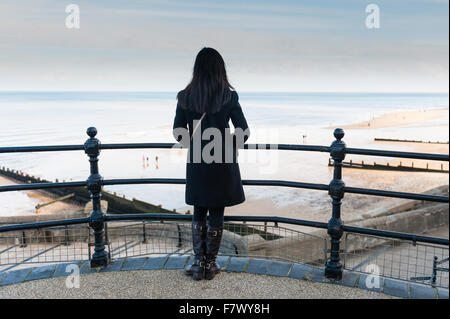 Une jeune femme donne sur la plage et la mer à partir du chemin à côté de la jetée de Cromer Norfolk, England UK Banque D'Images