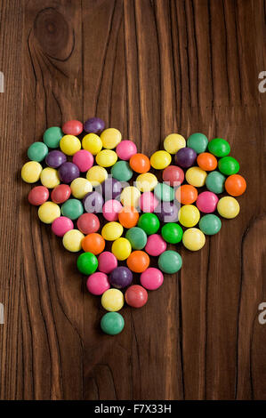 Bonbons colorés chute en forme de cœur sur un sol en bois Banque D'Images