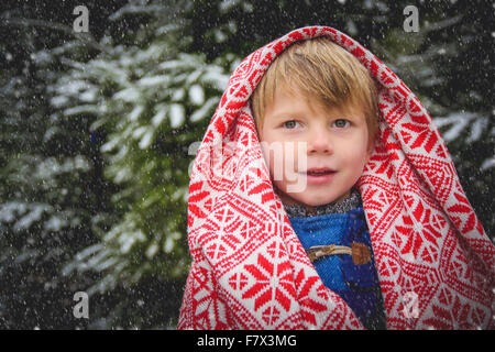 Portrait of smiling boy enveloppé dans une couverture dans la neige Banque D'Images