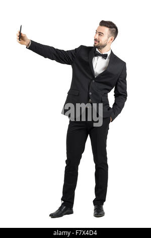 Jeune homme en costume avec nœud papillon en tenant avec selfies cellphone. La pleine longueur du corps portrait studio isolated over white background Banque D'Images