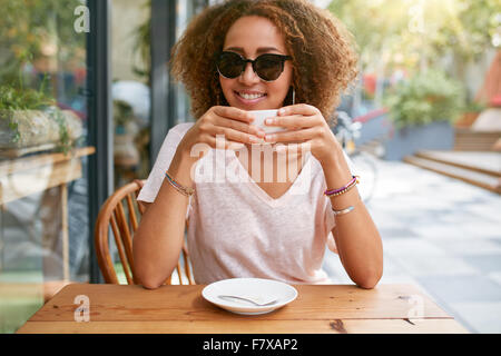 Portrait de jeune fille souriante de boire du café. Jeune femme africaine tenant une tasse de café à la caméra en souriant alors que sitti Banque D'Images