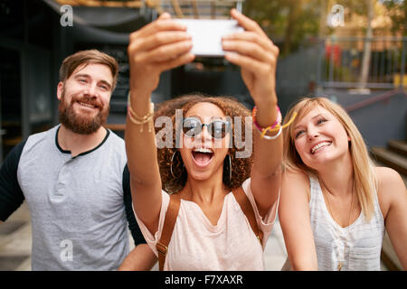 Group of smiling friends avec selfies téléphone mobile. L'homme et aux femmes de bénéficier d'multiraciale eux-mêmes à l'extérieur et de prendre pict Banque D'Images