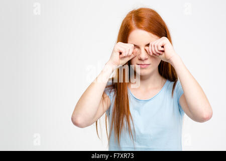 Sleepy assez jeune femme avec de longs cheveux rouges se frottant ses yeux par des mains isolated over white background Banque D'Images