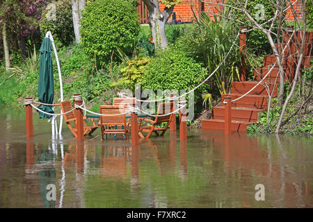 Une série de marches de bois qui mènent à des chaises en bois avec une table et un parasol en extérieur dans un jardin arrière demi couvert dans l'eau Banque D'Images