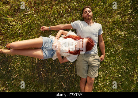 Jeune homme et femme couchée sur la pelouse de dormir. Vue de dessus de jeune couple ensemble au repos sur l'herbe. Banque D'Images