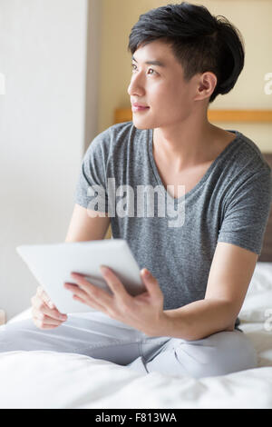 Young man using digital tablet on bed Banque D'Images