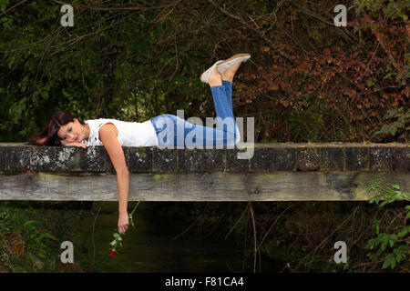 Belle femme couchée sur le pont de bois dans le parc avec rose rouge dans sa main. Banque D'Images