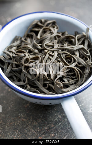 Noir avec des nouilles cuites squid encre sépia in colander Banque D'Images