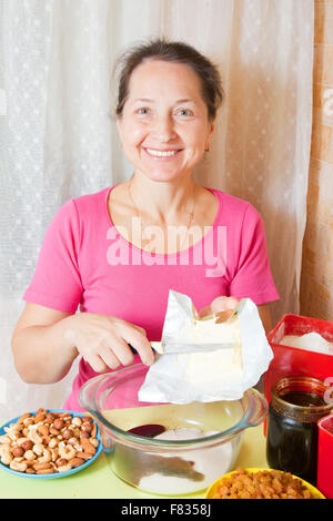 Femme mature ajoute la margarine dans le plat. L'une des étapes de la cuisson du gâteau au miel. Voir la série Banque D'Images