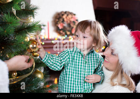 Garçon enfant contribue à sa mère et à son père pour décorer l'arbre de Noël de la famille Banque D'Images