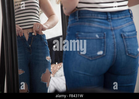 Une femme à la maison en tirant sur des jeans serrés devant un miroir de chambre à coucher. Banque D'Images