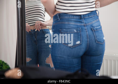 Une femme à la maison en tirant sur des jeans serrés devant un miroir de chambre à coucher. Banque D'Images