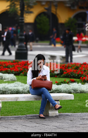 Fille assise sur un banc à l'aide de la messagerie mobile, Plaza de Armas, Lima, Pérou Banque D'Images