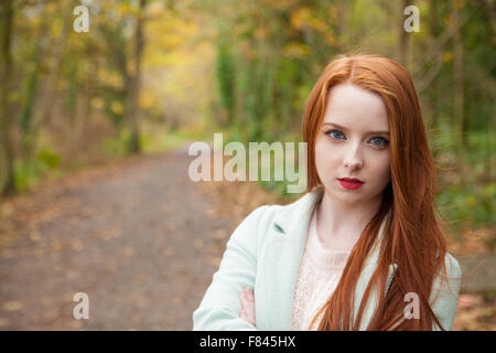 Femme rousse à l'extérieur avec un sentier dans la forêt en arrière-plan. Banque D'Images