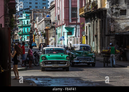 Une paire de voitures classique vert dans Centro Havana sortent de l'ombre exprimés par le soleil levant qu'ils avaient vers la vieille ville. Banque D'Images