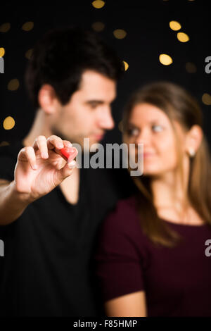 Jeune couple, homme et femme, sur fond noir, holding red heart Banque D'Images