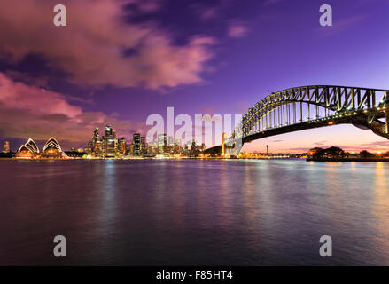 Principaux monuments de Sydney au coucher du soleil au port avec de l'eau brouillée et nuages reflétant les lumières vives de l'éclairage coloré Banque D'Images