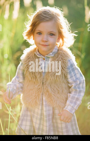 Cute smiling girl in a green field au coucher du soleil Banque D'Images