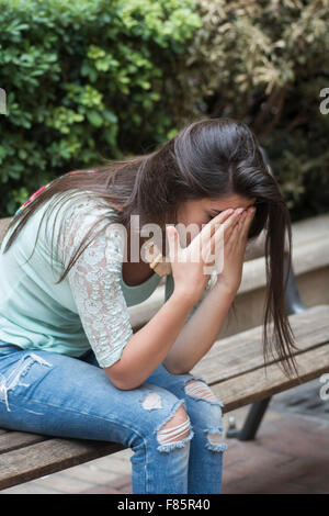 Souligné jeune femme assis sur banc de la tête dans les mains Banque D'Images