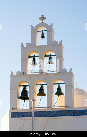 Santorin, Oia. Panaghia blanchis à Platsani église orthodoxe grecque, clocher, avec trois pneus de cloches, d'un rétro-éclairage par heure d'or du soleil. Banque D'Images