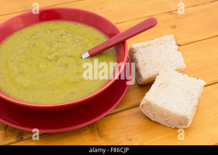 Soupe aux pois et jambon dans un bol rouge, servi avec des morceaux de pain blanc frais Banque D'Images