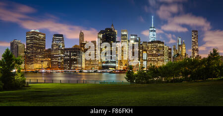 Soir vue de Lower Manhattan gratte-ciel lumineux à travers Brooklyn Bridge Park. Le Quartier Financier de Manhattan, New York City Banque D'Images