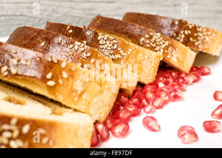 Rouleau de tranches de gâteau au sésame sur le dessus et les graines de grenade fraîche sur plaque blanche avec fond texturé en bois. Banque D'Images