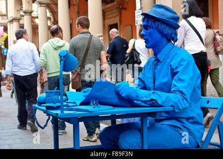 Homme peint en bleu interprète de rue, statue humaine, assis encore à un bureau, dans une rue animée. Bureau dans la rue. Bologne, Emilie Romagne, Italie, UE Banque D'Images