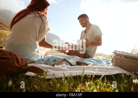 Jeune homme de verser le vin dans les verres, en position assise avec sa petite amie. Jeune couple boire du vin et d'apprécier un pique-nique en plein air. Banque D'Images