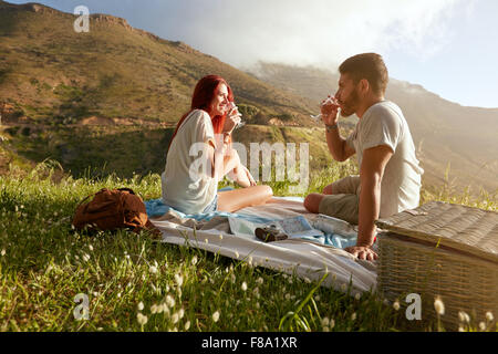 Tourné en plein air d'un jeune couple drinking wine. L'homme et la femme détendue sur les vacances d'été en campagne. Banque D'Images