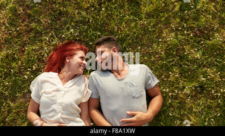Vue supérieure de l'heureux jeune couple dans l'amour de vous détendre sur l'herbe. Young man and woman lying on grass looking at ea Banque D'Images