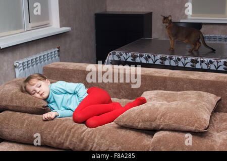 Montres cat petite fille dort comme un haut sur un canapé Banque D'Images