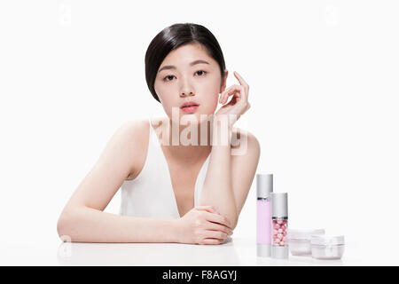 Young Asian woman assis à la table pliante et un bras avec l'autre main sous son visage avec des produits de beauté sur la table Banque D'Images