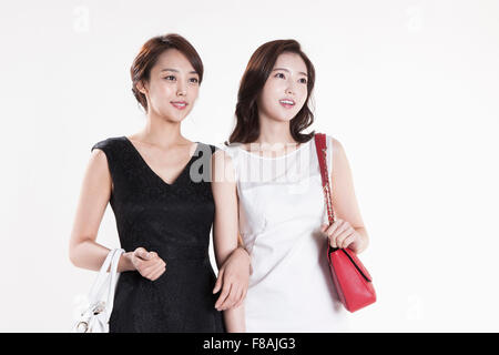 Deux smiling Asian femmes avec leurs sacs à main reliant leurs bras regardant fixement vers le haut Banque D'Images