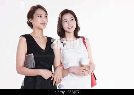 Deux smiling Asian women avec leurs sacs à main et le café dans une main de femme vêtue de blanc qui relie leurs bras fixant Banque D'Images