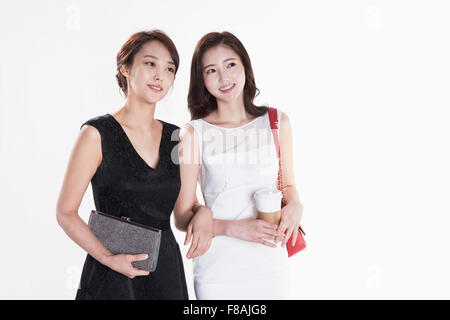 Deux smiling Asian women avec leurs sacs à main et le café dans une main de femme vêtue de blanc qui relie leurs bras fixant Banque D'Images