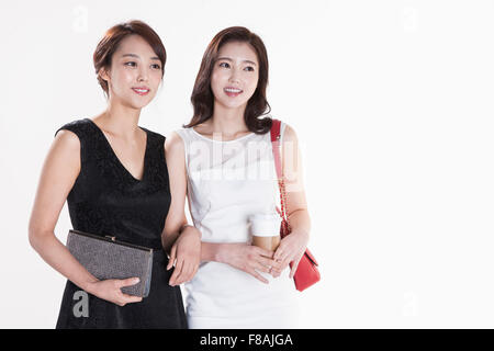 Deux smiling Asian women avec leurs sacs à main et le café dans une main de femme vêtue de blanc qui relie leurs bras fixant Banque D'Images