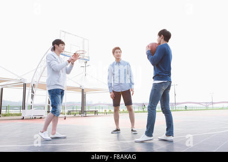 Trois jeunes hommes debout à la cour de basket-ball Banque D'Images