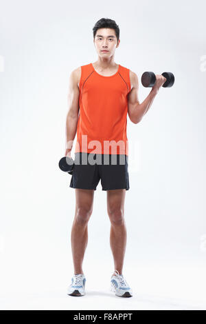 Homme confiant dans les vêtements de sport holding dumbbells regarder/ Banque D'Images