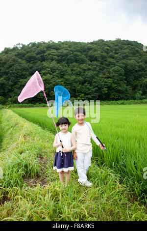 Smiling boy and Girl standing avec des filets à regarder avant sur lane à travers les champs de riz au printemps Banque D'Images