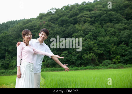 Smiling couple holding hands en plaçant la main sur l'épaule contre les champs de riz et la montagne au printemps Banque D'Images