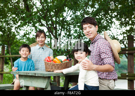 Portrait de famille heureuse assis autour d'une table à l'air libre avec des légumes frais à regarder/ Banque D'Images