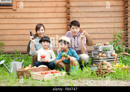 Smiling family sitting avec des légumes frais en maison de yard à regarder/ Banque D'Images