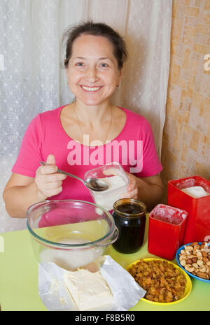 Femme mature ajoute le sucre en plat à la table de cuisine. L'une des étapes de la cuisson du gâteau au miel. Voir la série Banque D'Images