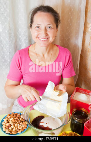 Femme mature ajoute la margarine dans le plat. L'une des étapes de la cuisson du gâteau au miel. Voir la série Banque D'Images