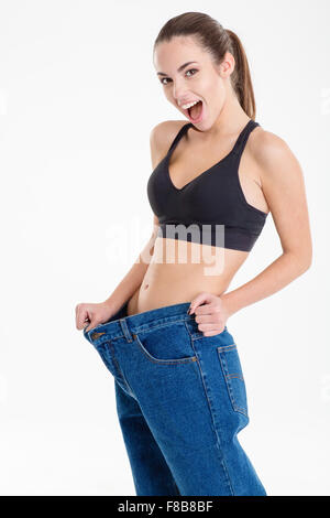 Surpris jeune femme fitness est devenu vieux jeans skinny et portant sur fond blanc Banque D'Images