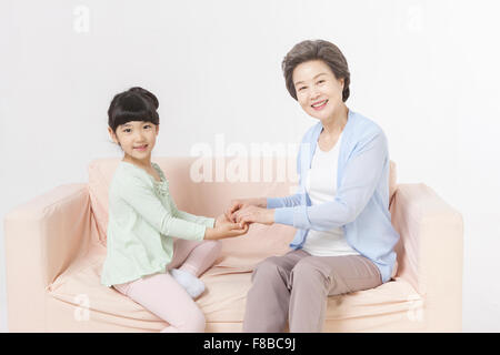 Grand-mère et petite-fille tenant leurs mains et en regardant de l'avant les deux assis sur un canapé Banque D'Images