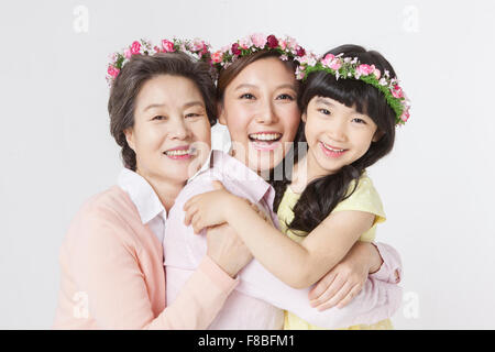 Mère, fille, grand-mère serrant les uns les autres et souriant de l'avant avec des couronnes de fleurs sur la tête Banque D'Images